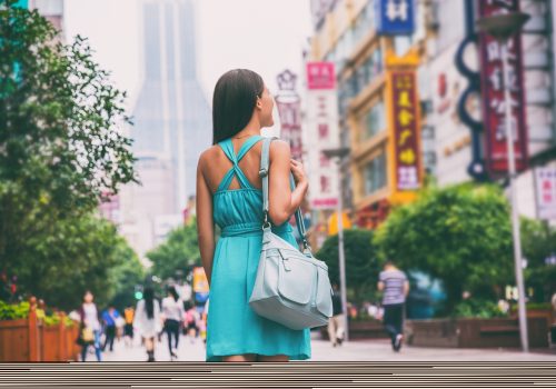 Shanghai city travel lifestyle shopping woman walking on Nanjing Road shop street, China, Asia. Asian girl with purse on urban adventure, famous chinese attraction landmark.